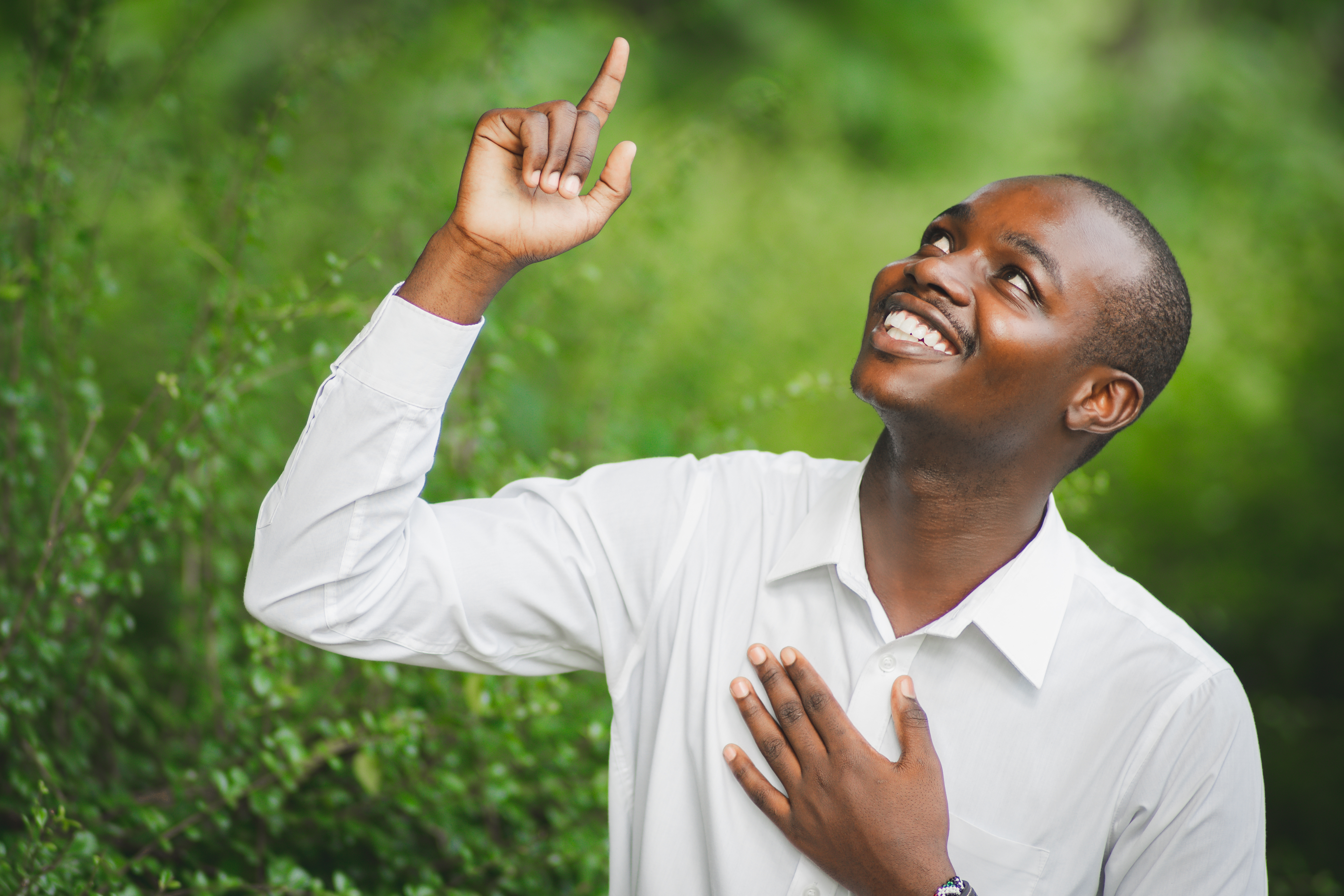 Man in white shirt pointing up and smiling gratefully